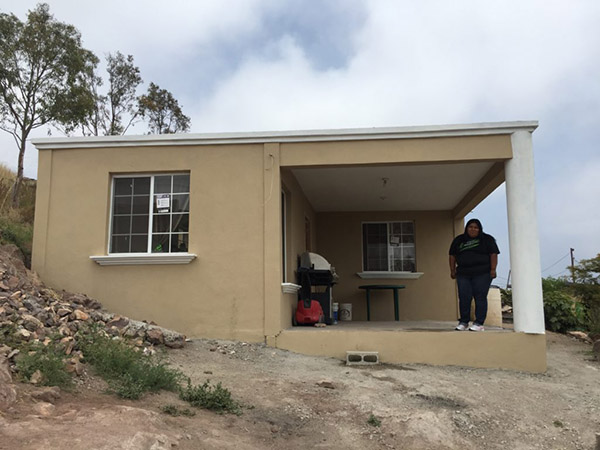 Belen standing at the entrance of her new home, painted beige and with a concrete awning