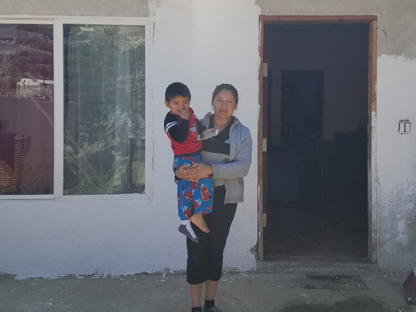 Liz stands holding her son at the entrance of her current home