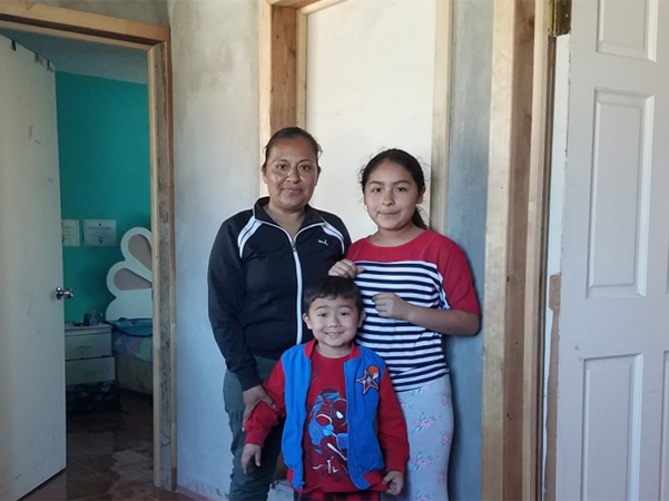 Olga and her 2 kids stand at the entrance of their home