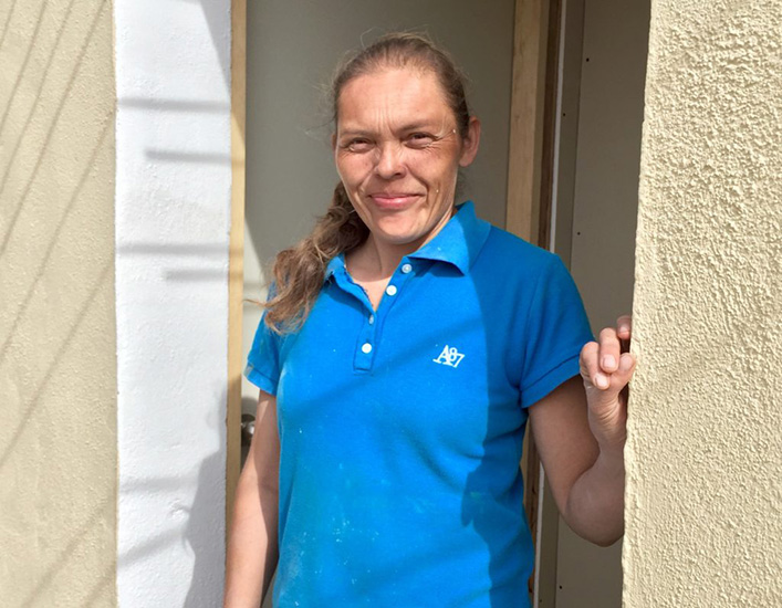 Rosie, wearing a blue shirt, poses at the entrance of her new home