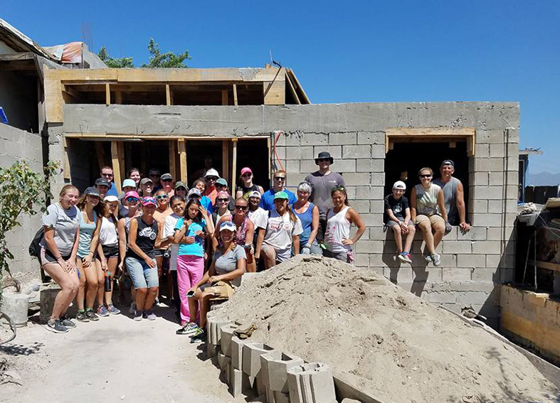 Trinity Lutheran intergen volunteer group poses with family in front of house framed and ready for the roof
