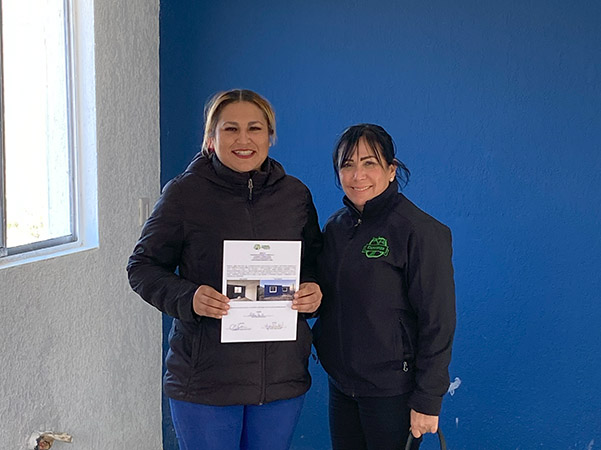 Adilene holds home certificate next to Cuquis, both inside her new home, one wall painted bright blue