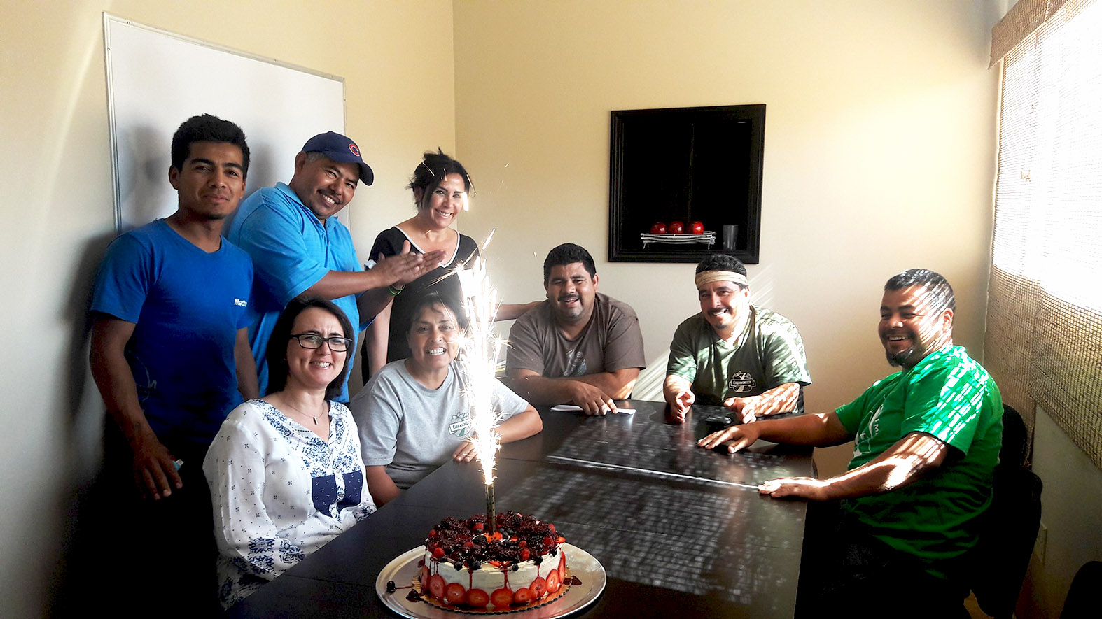 The Tijuana Esperanza team celebrates around a birthday cake with a firework candle in a cake