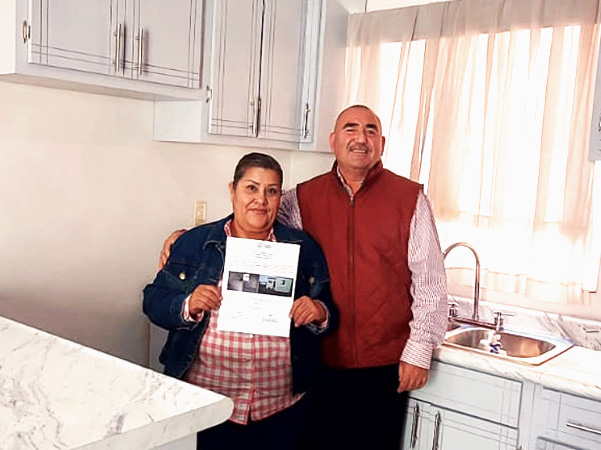 Couple stands holding certificate to their new home, standing inside their new completed white kitchen
