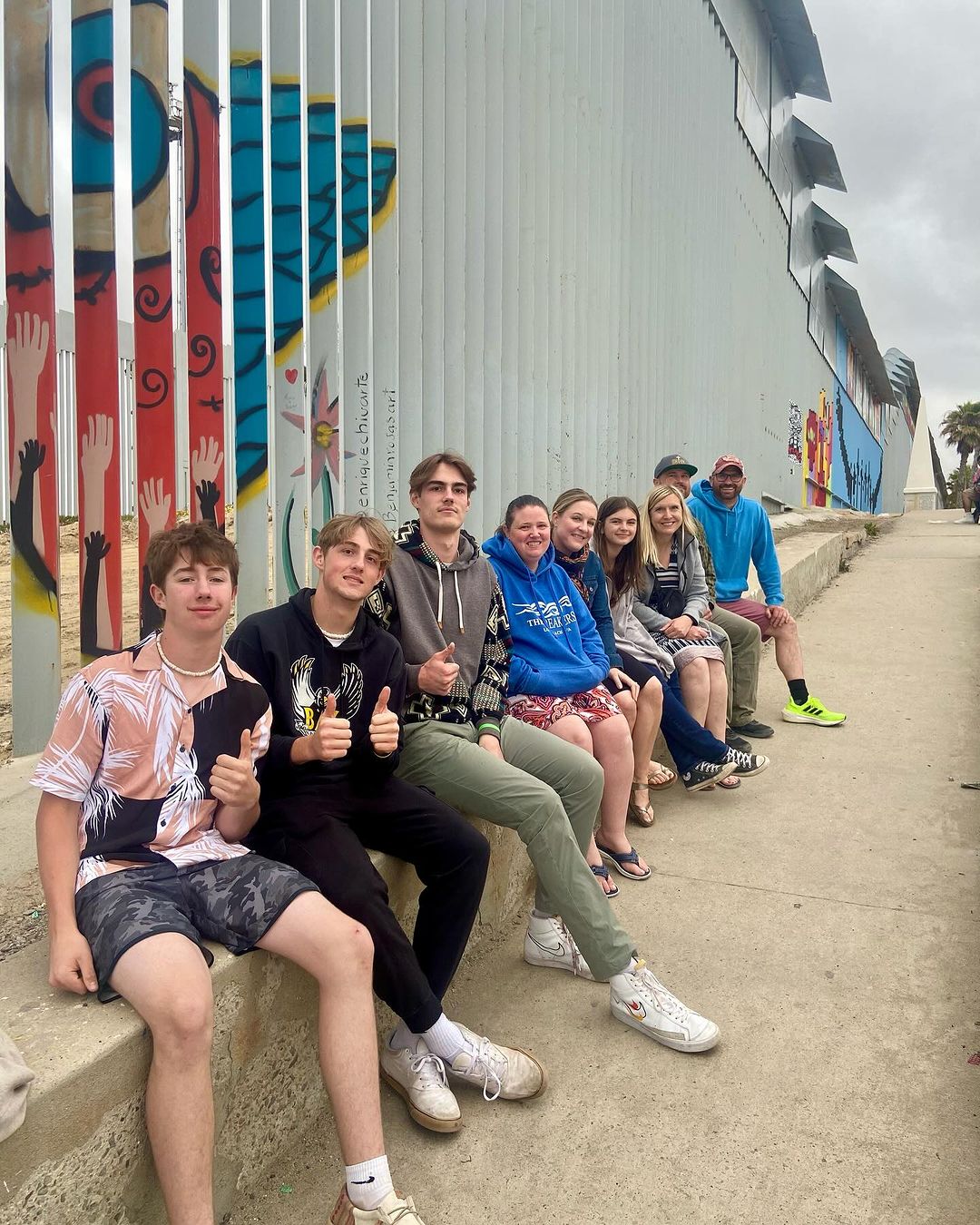 Group line up along slatted Tijuana border wall at El Bordo