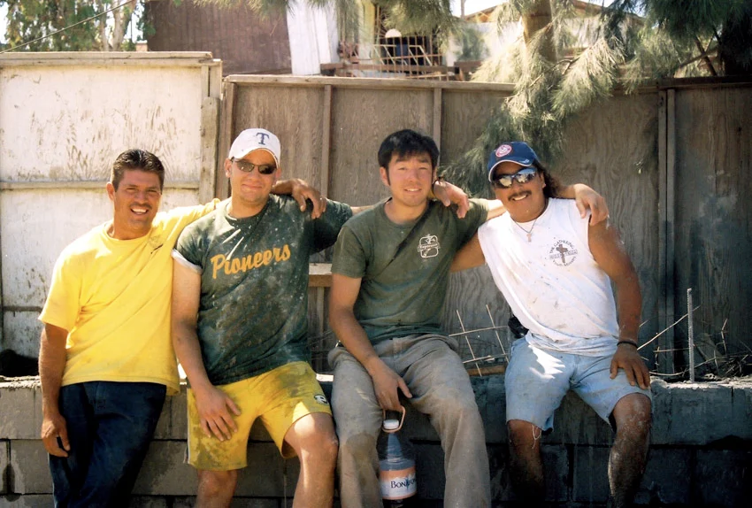 4 men sit arm in arm smiling at a worksite, including Steve a white man, Eduardo a mexican man, and two others