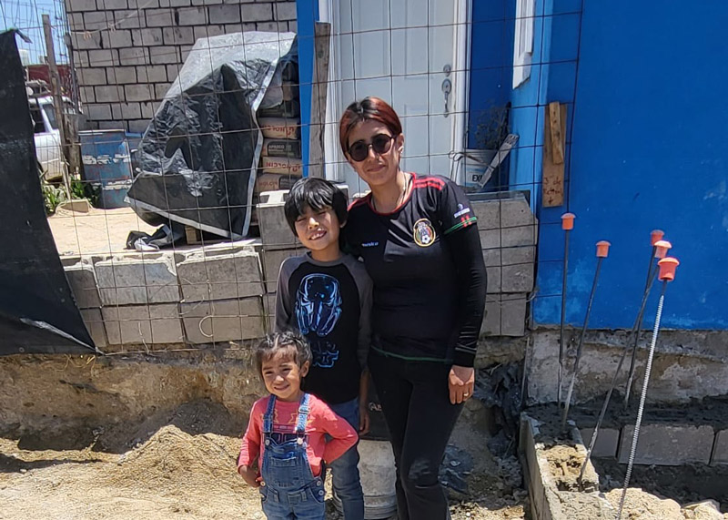 Karla and her young daughter smile and pose in front of a bright blue Esperanza house