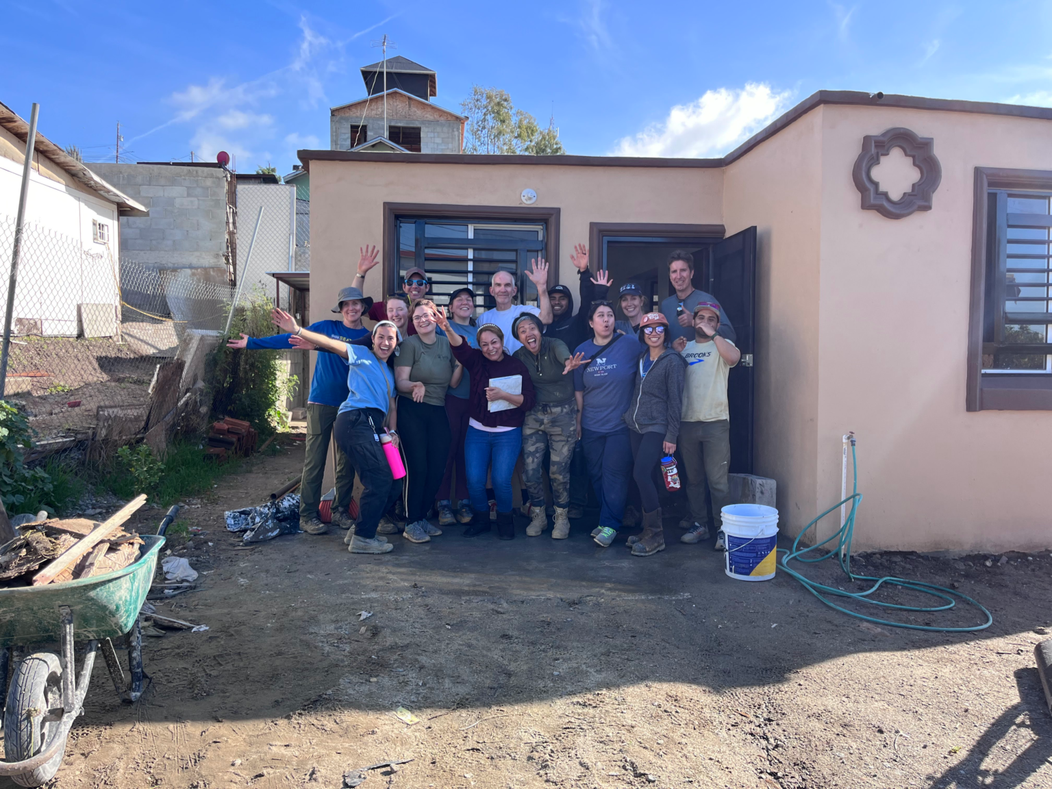 a group of adult volunteers with the woman home owner in the center stand excitedly in front of the completed home