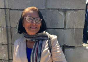 Angeles, a middle aged latina poses in front of concrete block wall of a future home