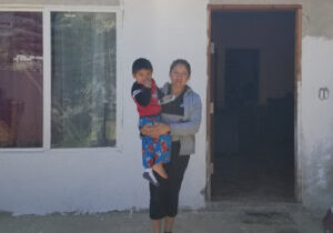 Liz stands holding her son at the entrance of her current home